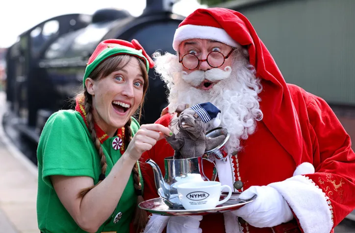 Santa and an elf standing on a train platform beside train carriages
