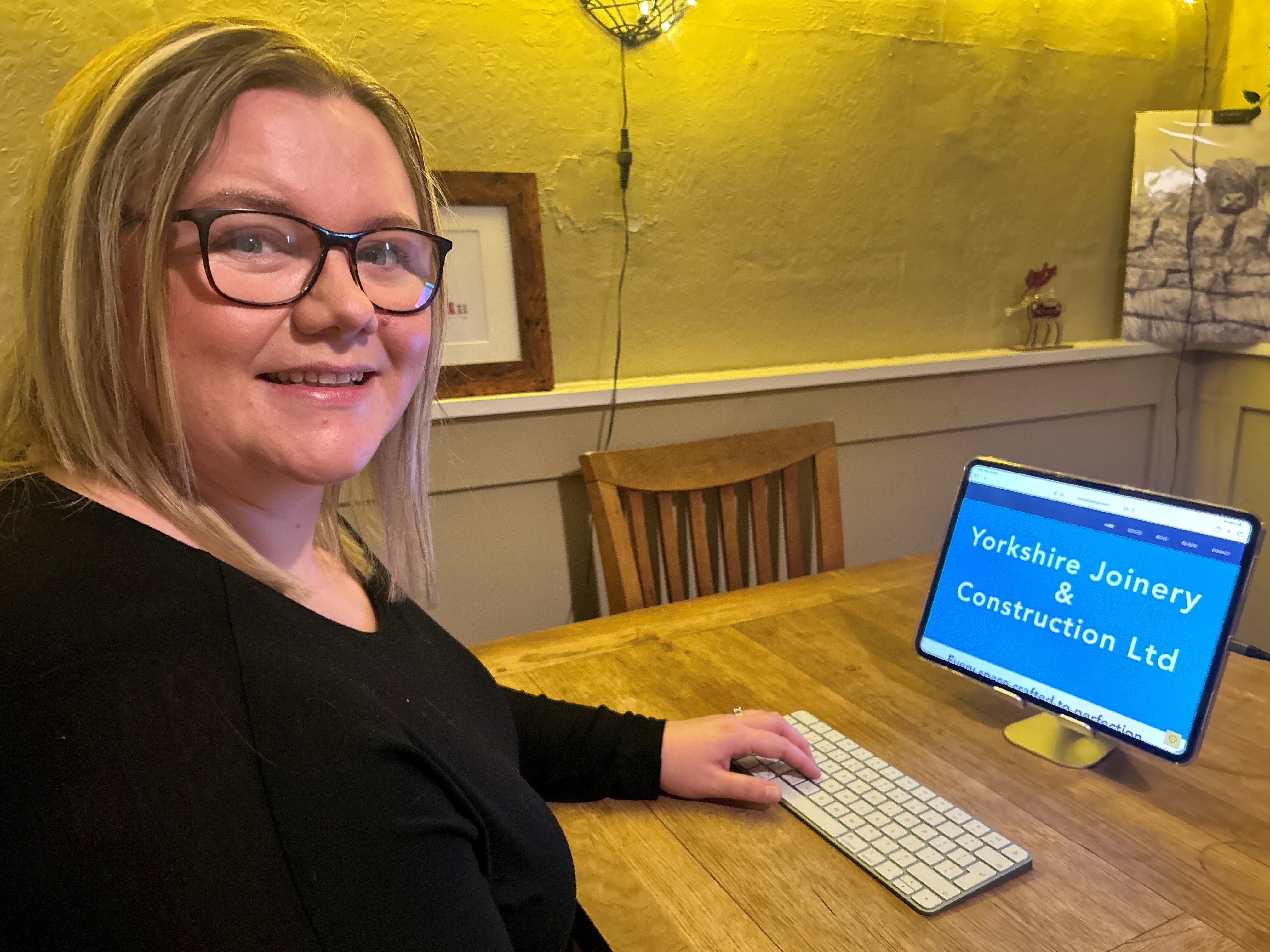 Adult sitting at a wooden table in front of monitor with her hand on keyboard