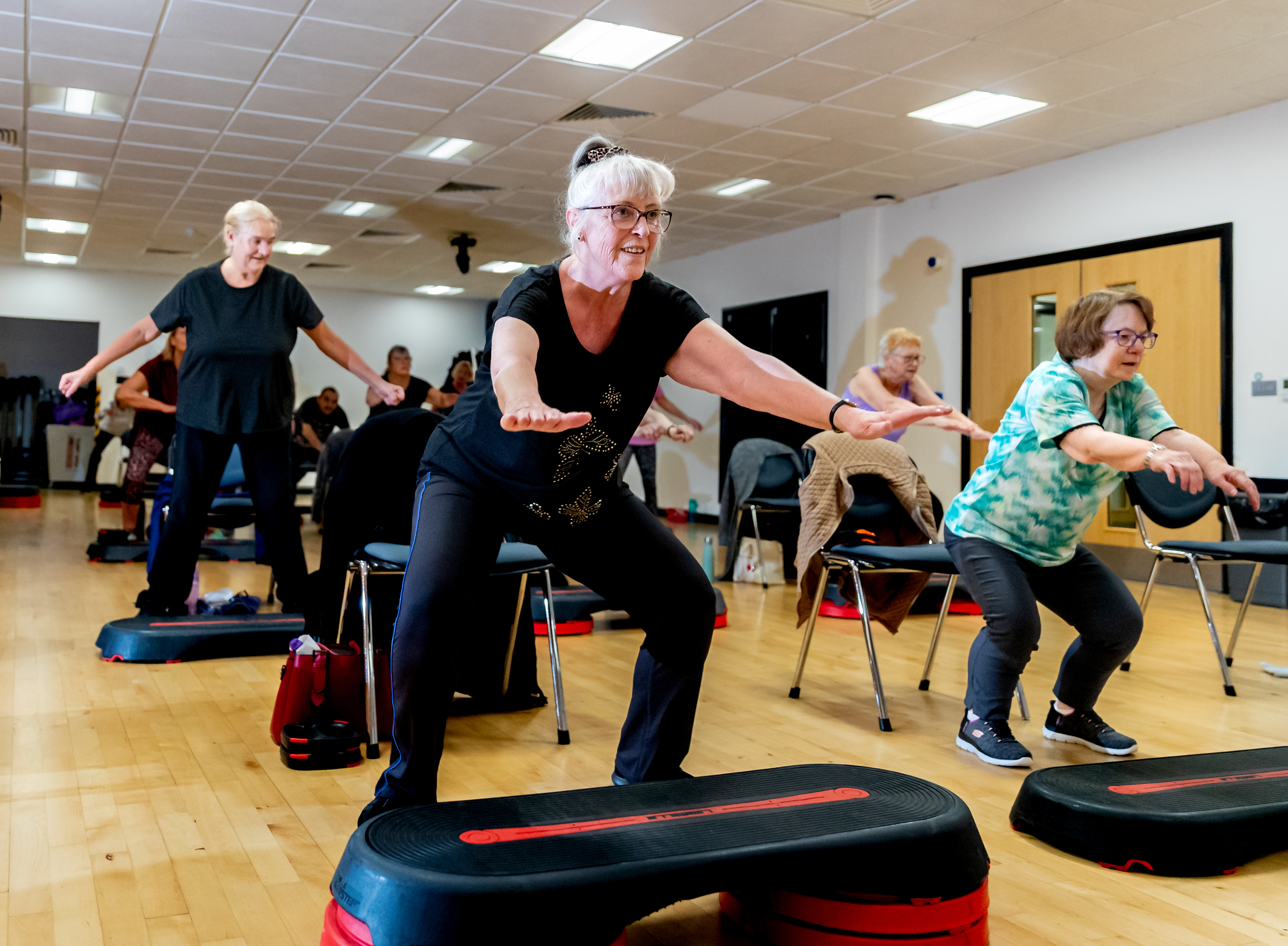 A group take part in a balance class, some are squatting down, some are standing on raised platforms.