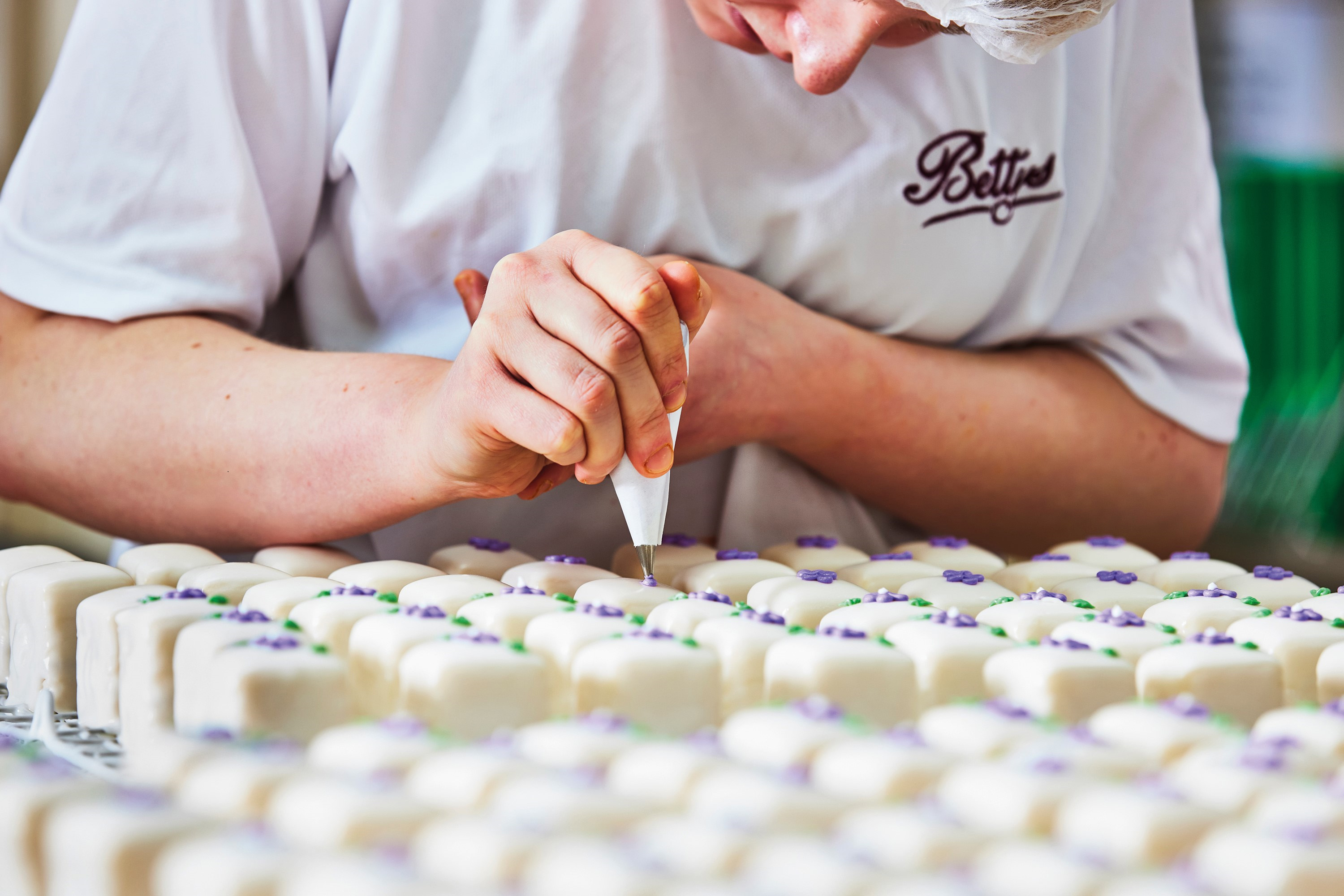 An adult wearing a Bettys uniform piping mini cakes