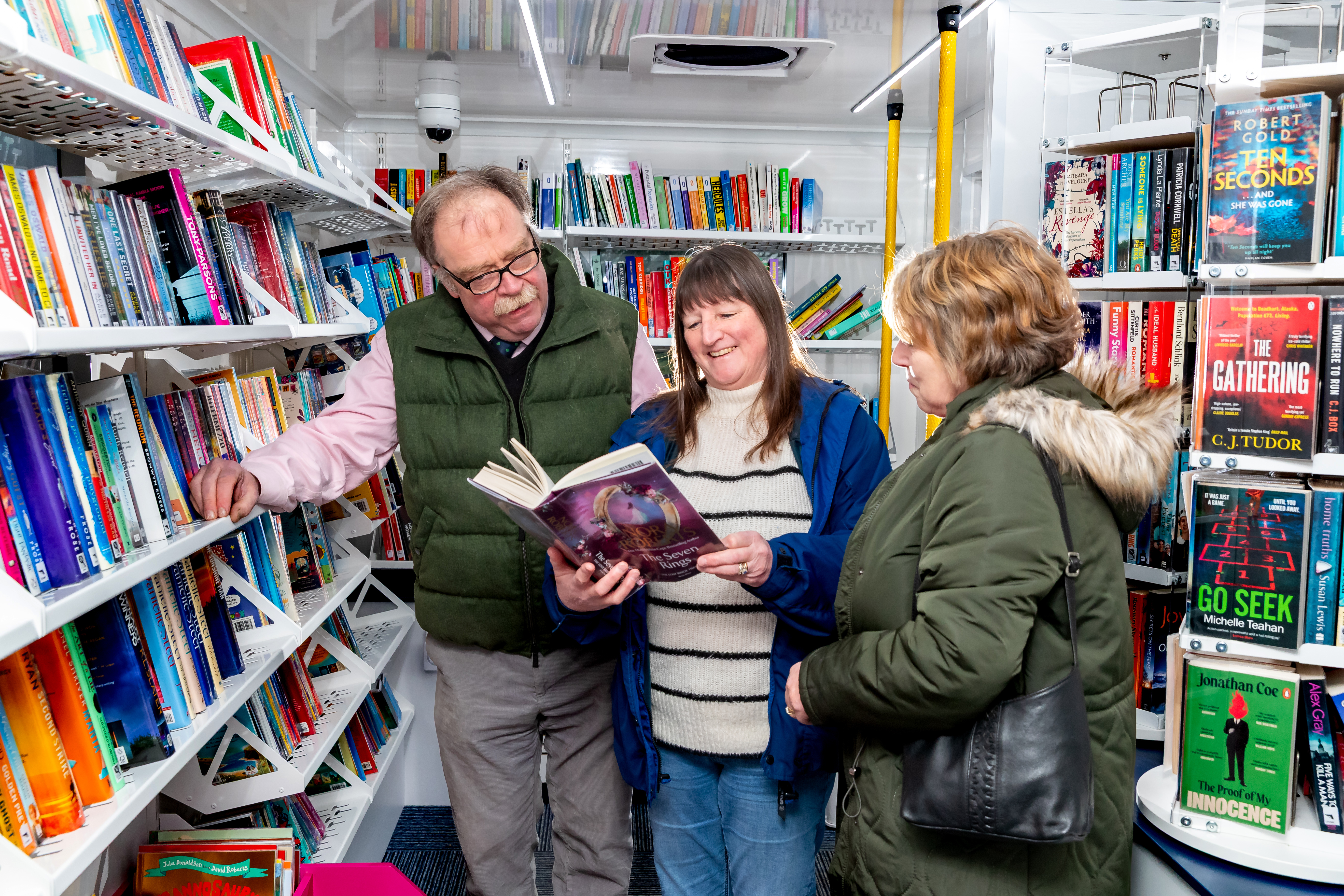 Three people looking at a book surrounded by books on shelves inside the new mobile libary.