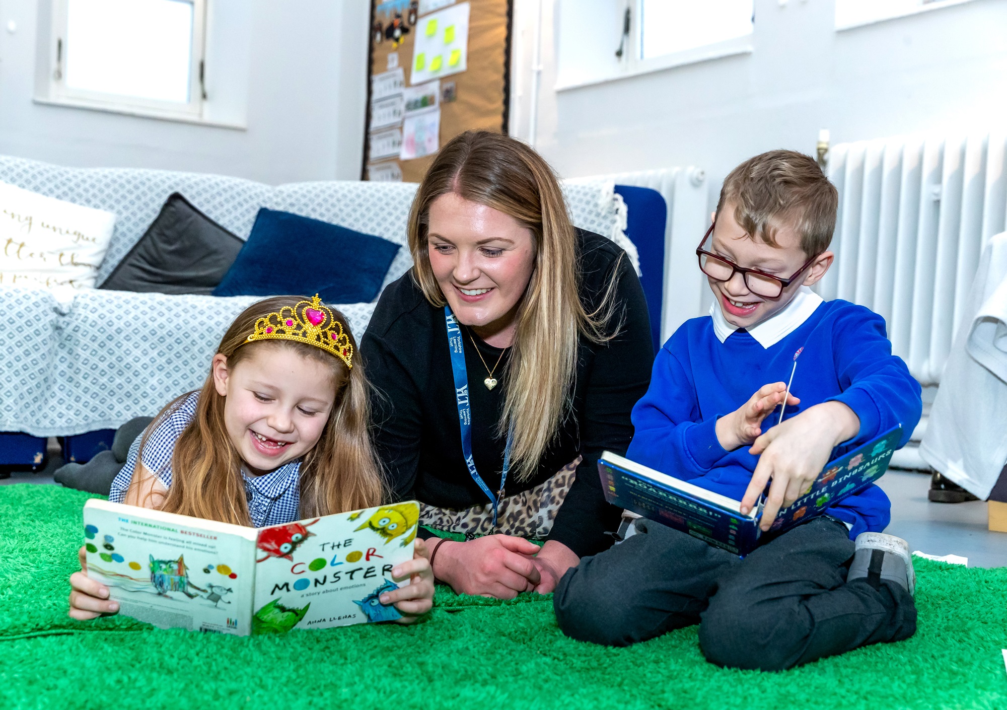A teacher with two children both of whom are reading books. 