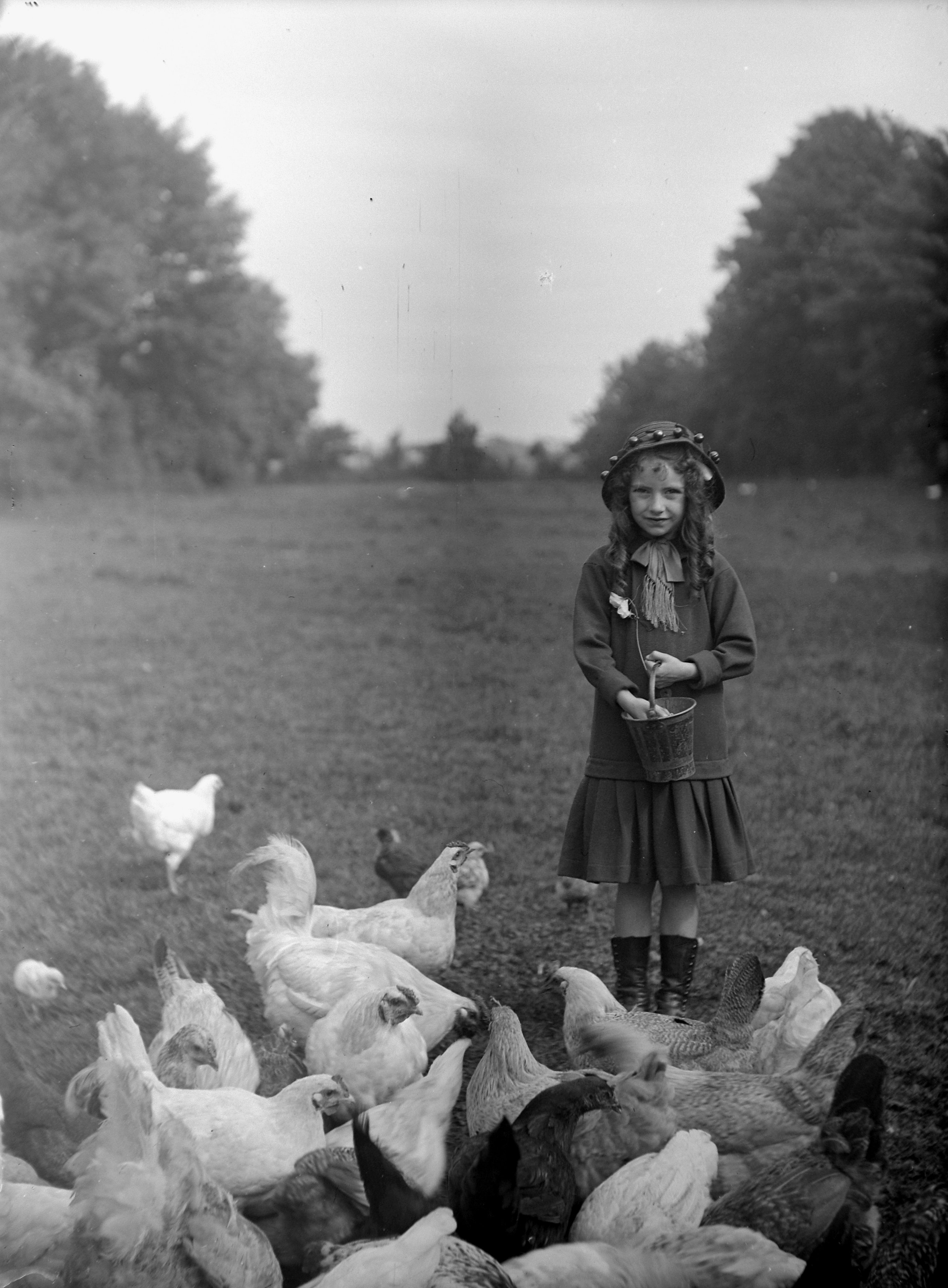 Black and white photo showing a lady feeding hens (1915). From a collection of photographs of the Dunsforth area by local amateur photographer Louisa Kruckenberg.