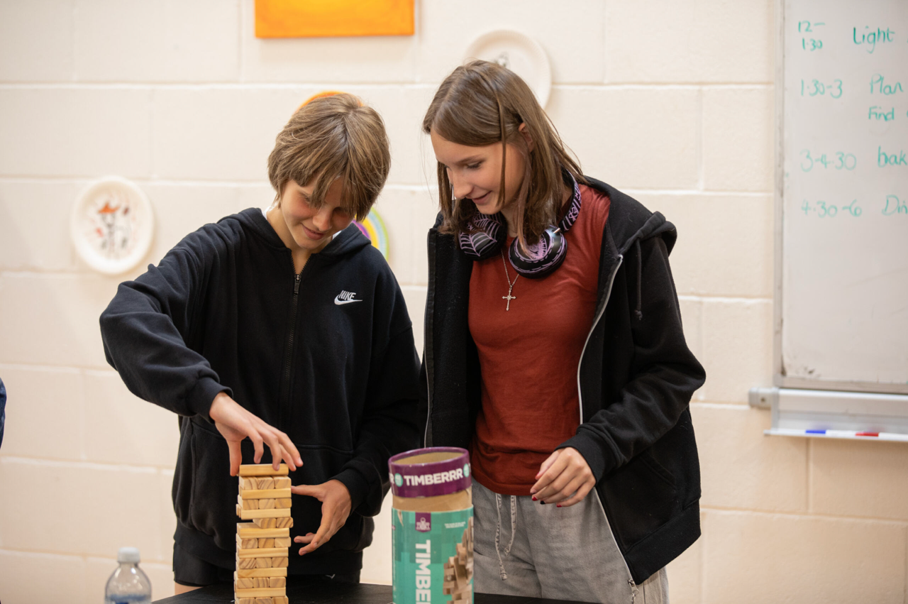 Two young adults standing playing a game of jenga on a small square table