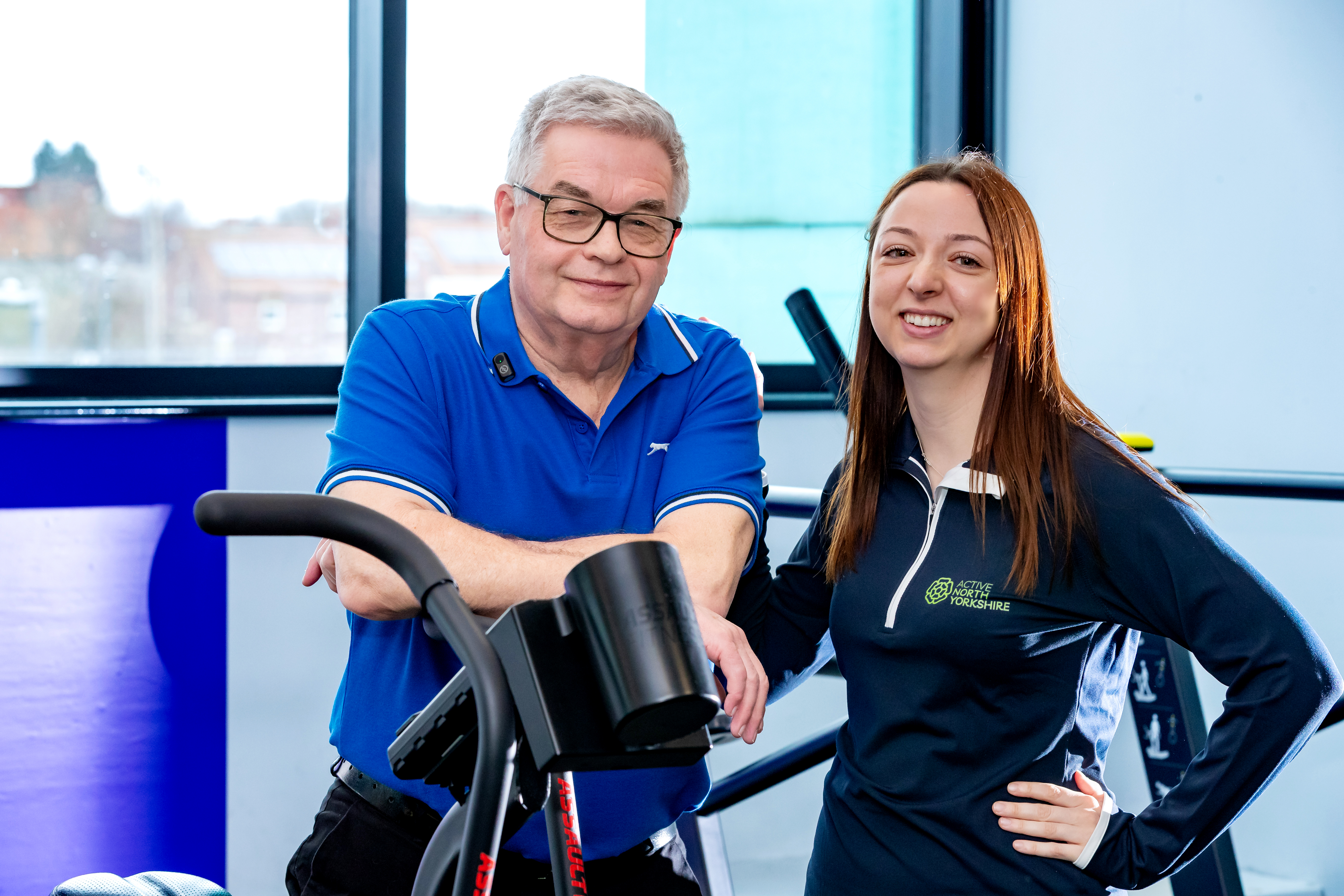 Two adults standing beside each other behind a piece of exercise equipment