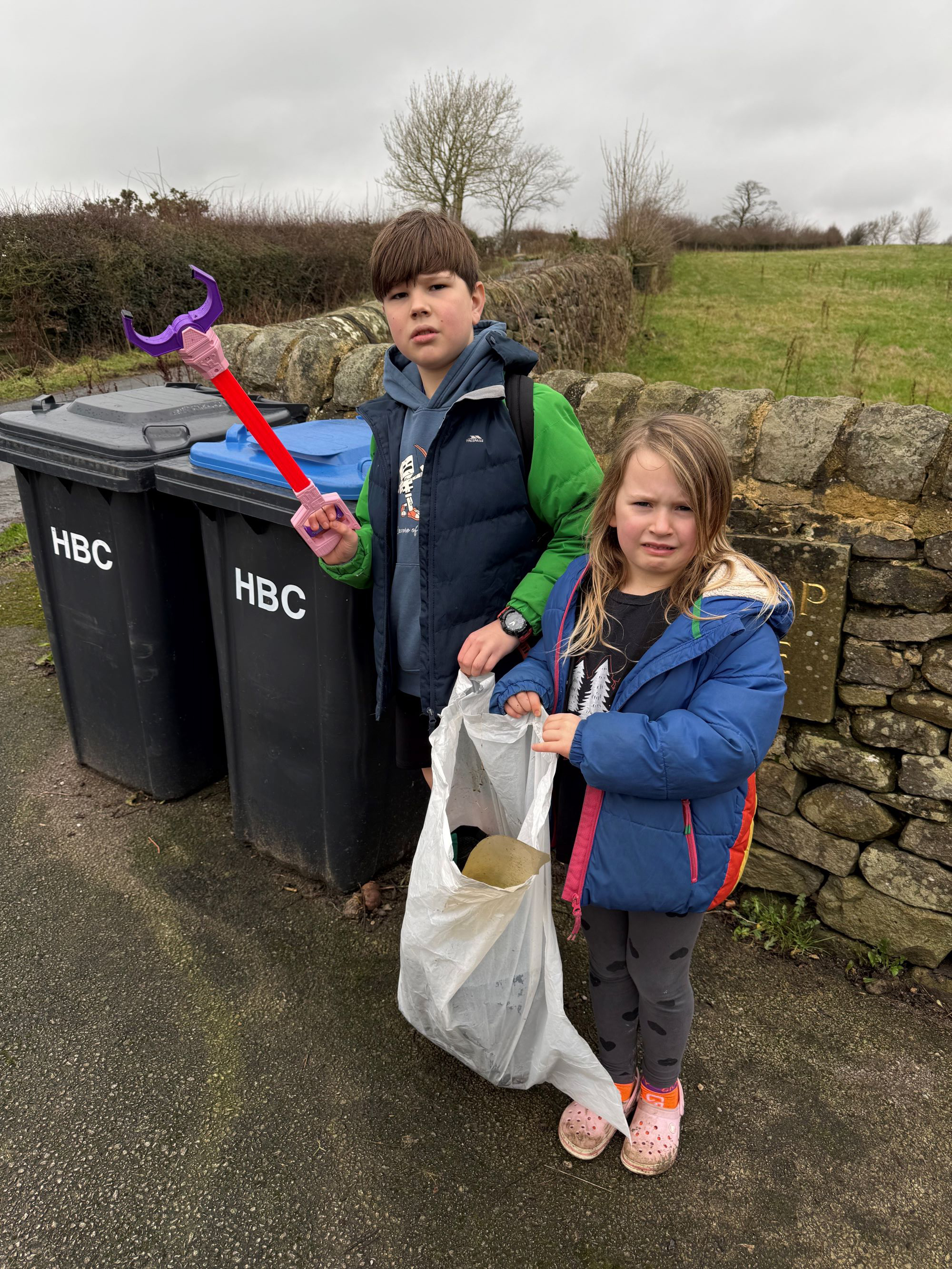 Two children with litter pickers in front of bins