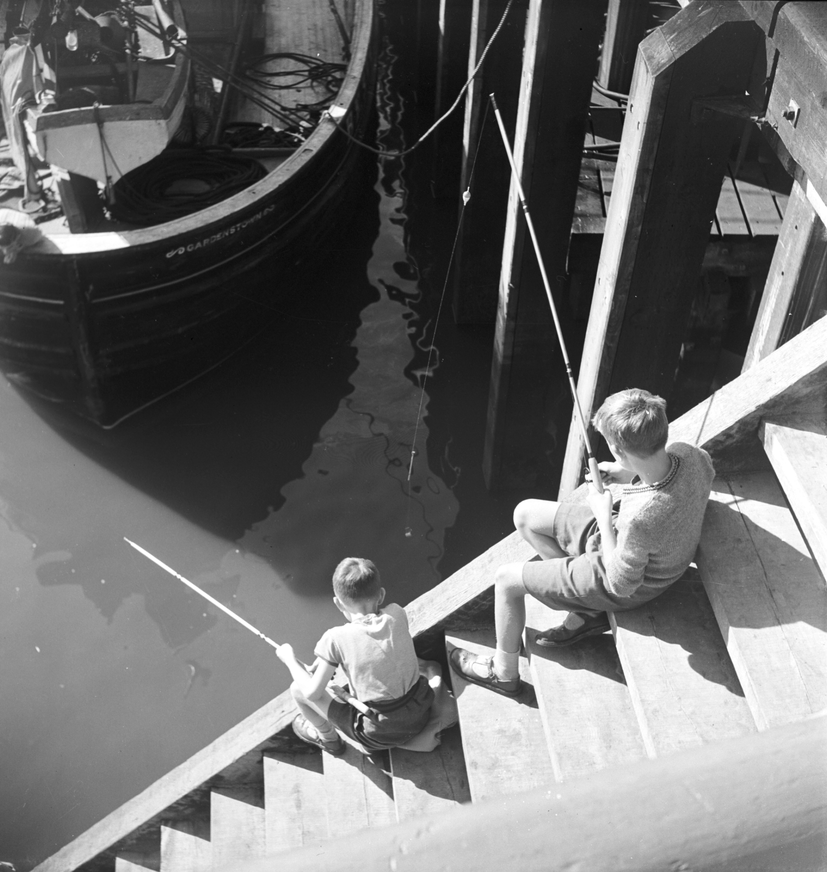 Black and white photo of two boys fishing at Whitby Harbour in the 20th century. From the Bertram Unné photographic collection.