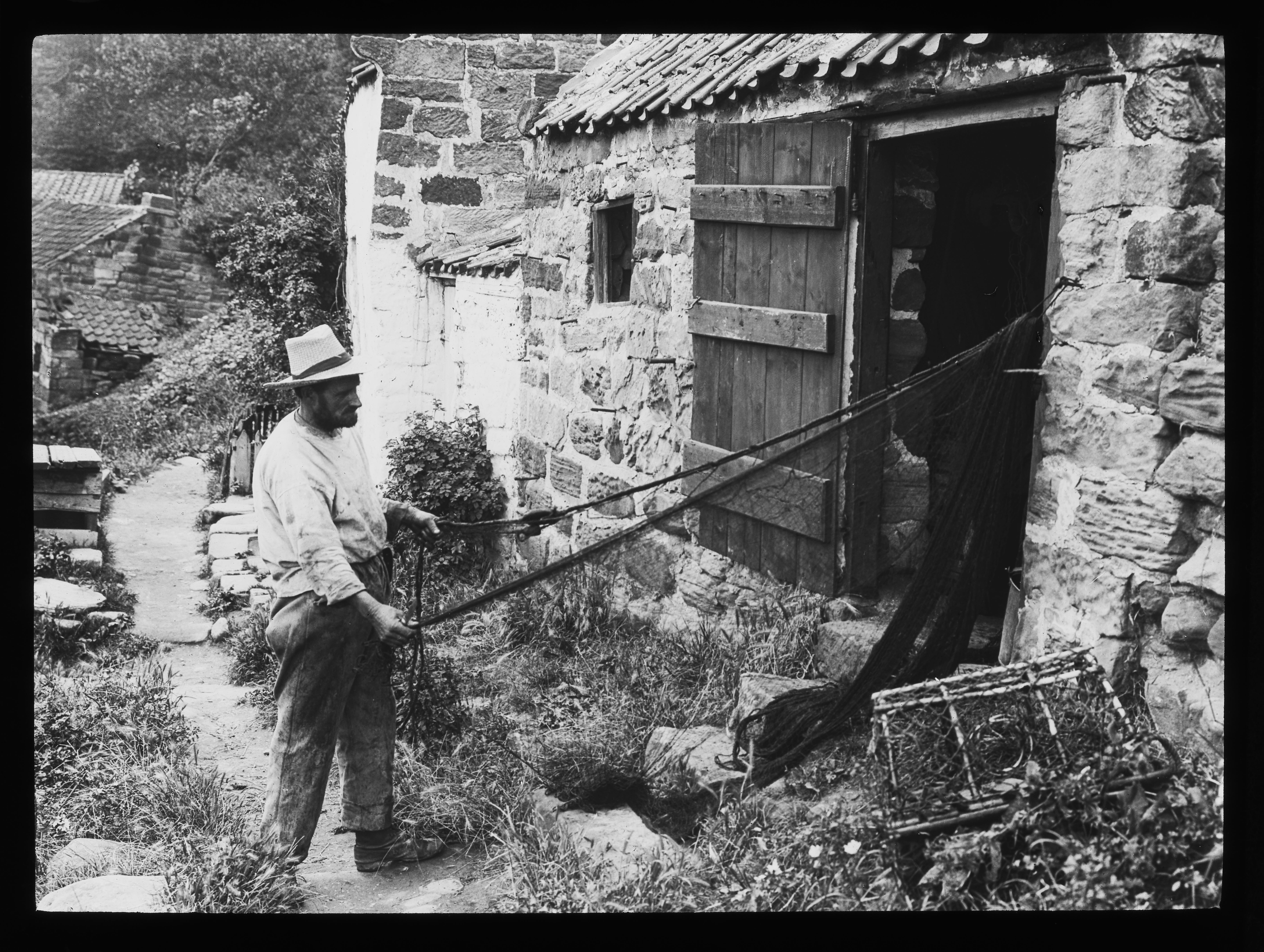 Black and white photo of a fisherman from Runswick Bay sorts his fishing nets and creels during the late 19th century. Photograph by Graystone Bird, from the ‘Tour of Yorkshire: coast’ photographic collection.