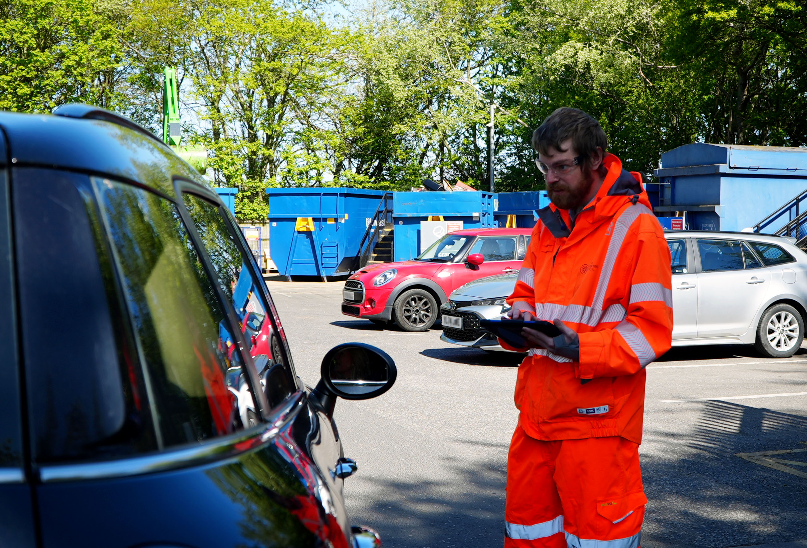 A man in hi viz checking car registration numbers at recycing centres