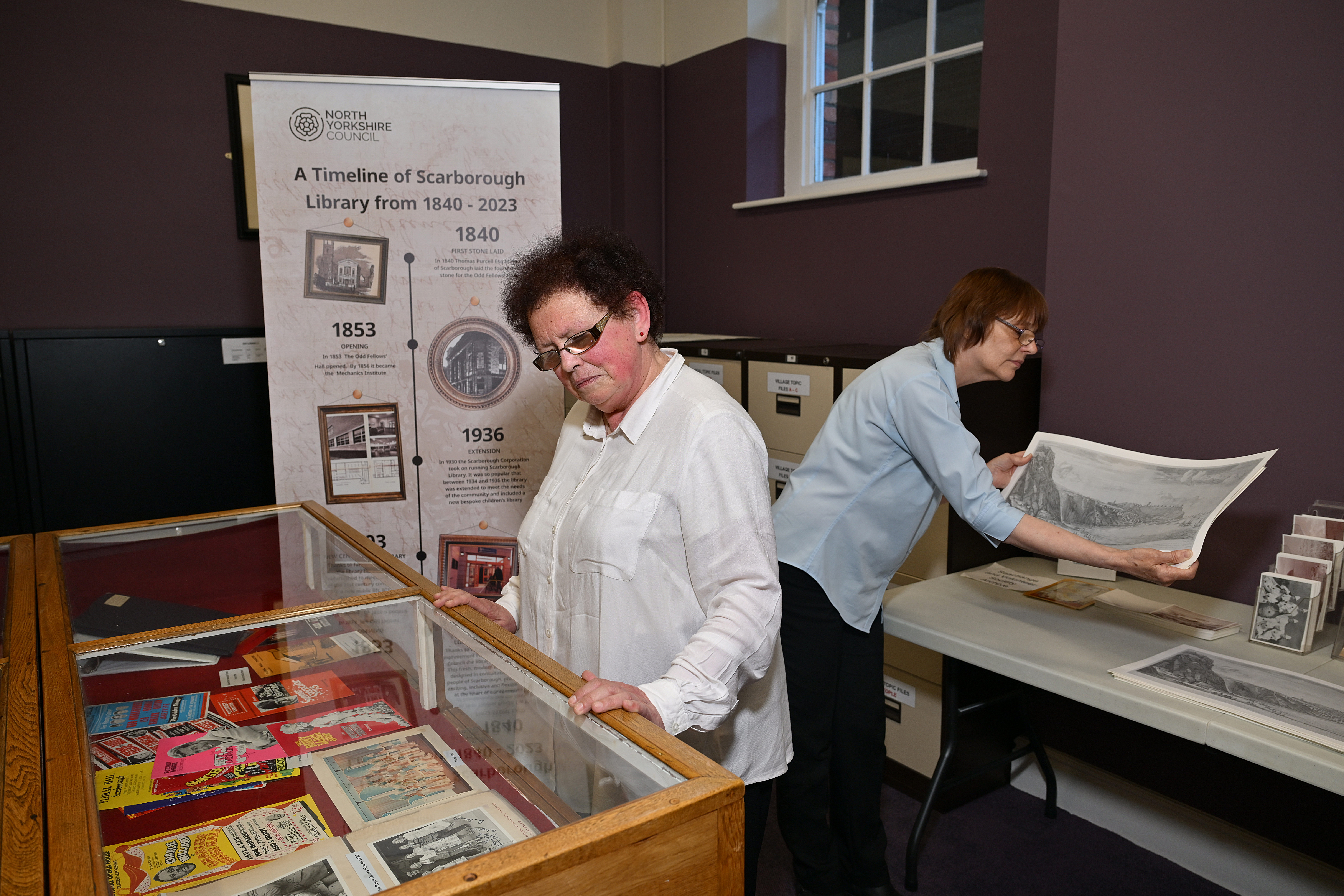 Two adults, one looking into a glass top unit at programmes and another looking at a black and white picture