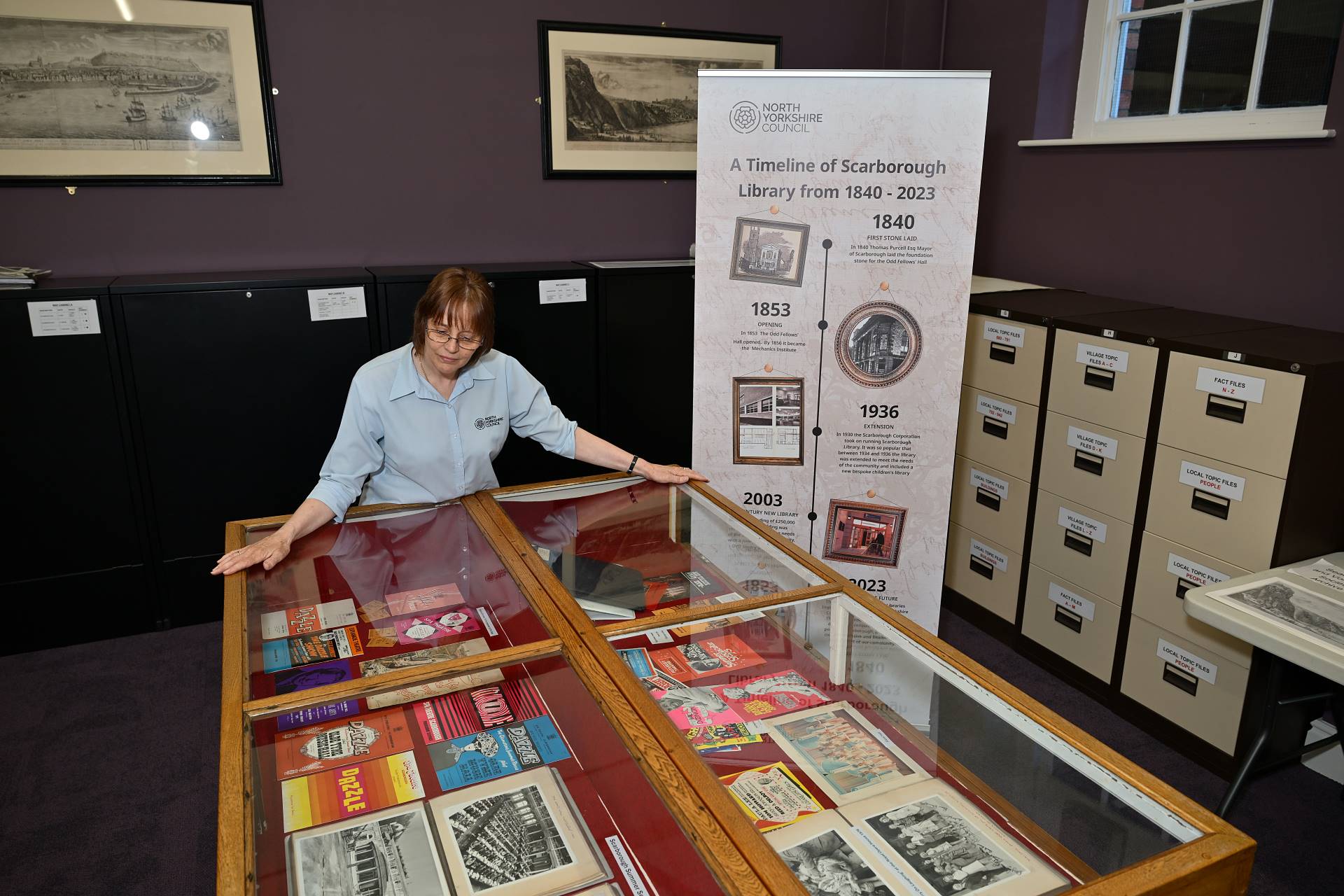 Adult standing looking into glass cabinet which displays programmes from past events and exhibitions