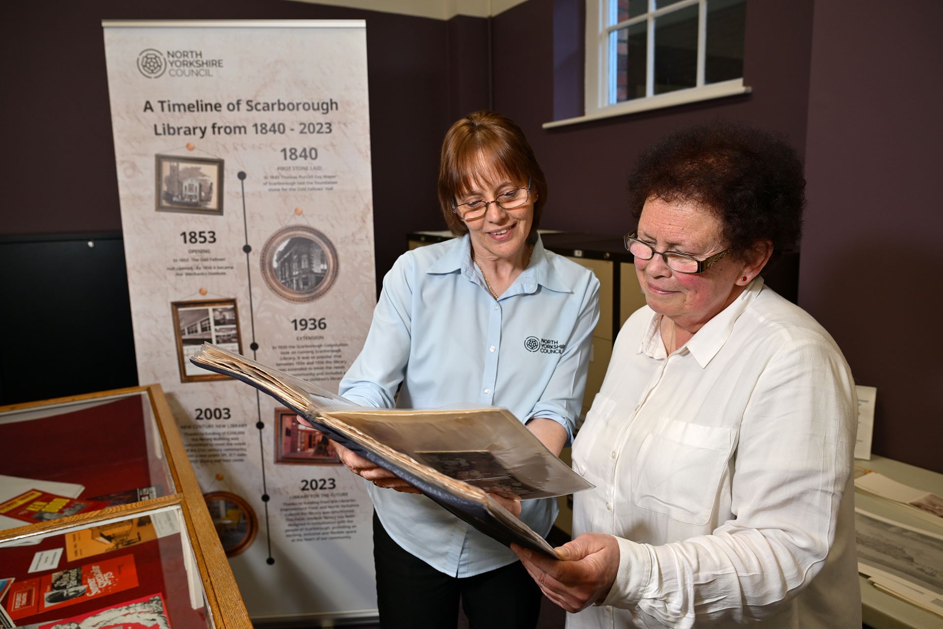 Two adults standing together looking at a large album with a pull up banner behind them
