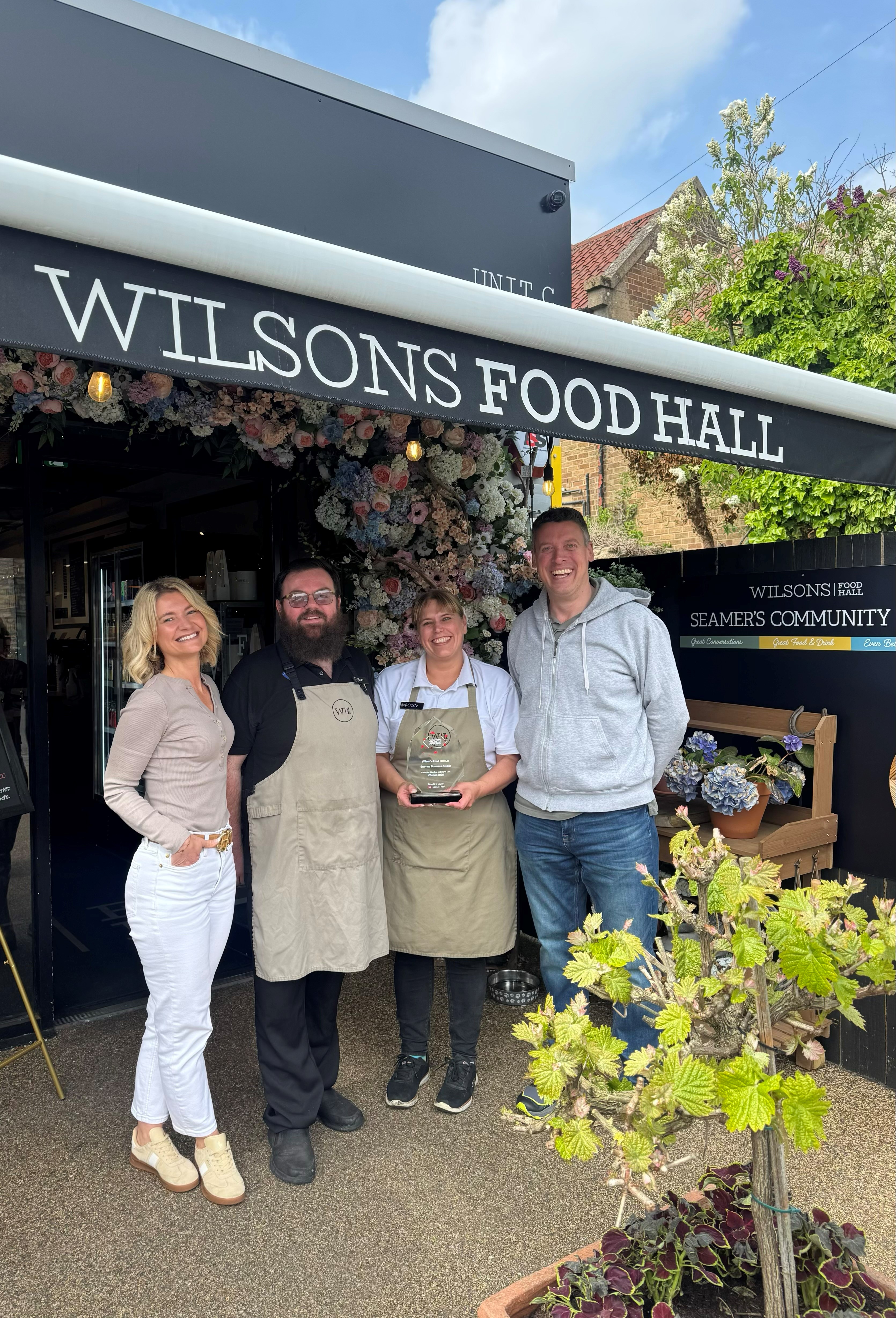 Group of people smiling standing underneath the Wilsons Food Hall canopy