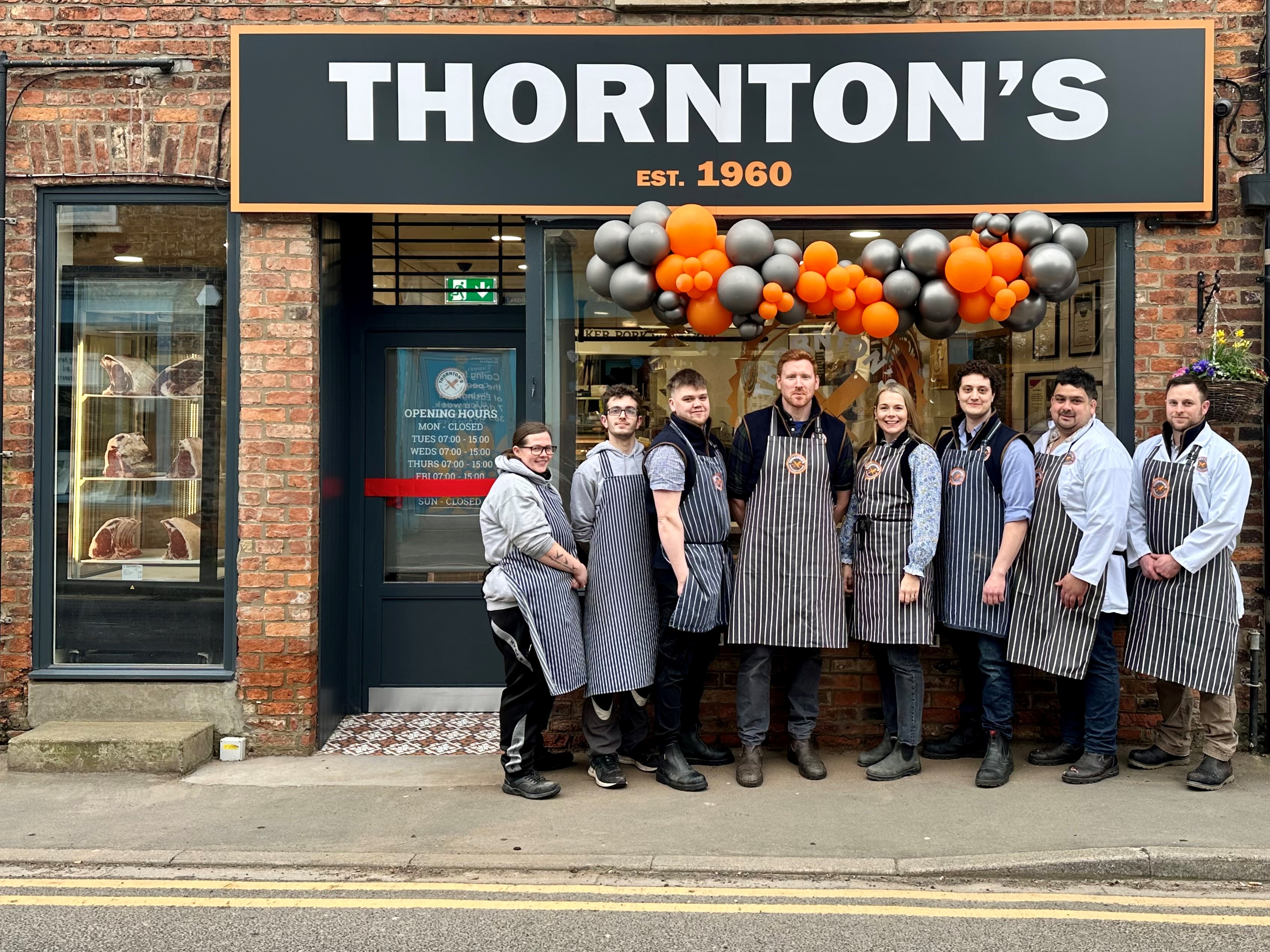 Group of people standing outside Thornton's shop with orange and silver balloons above them