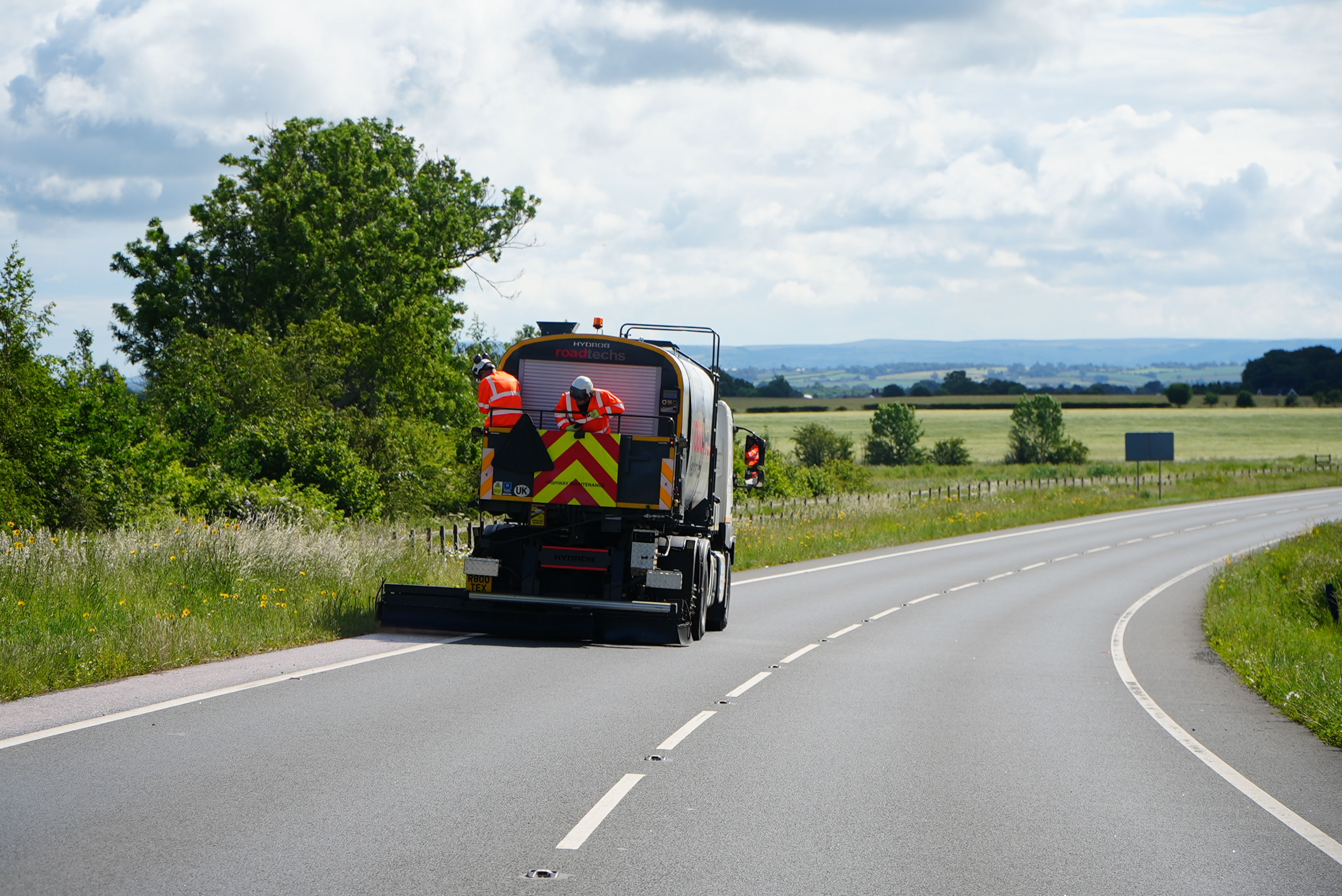 Highways vehicle working on a road with two members of the highways team standing at the back of the vehicle
