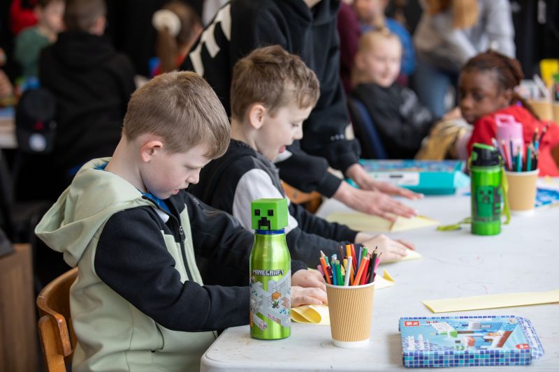 A small group of children sitting at a table a colouring and making paper airplanes