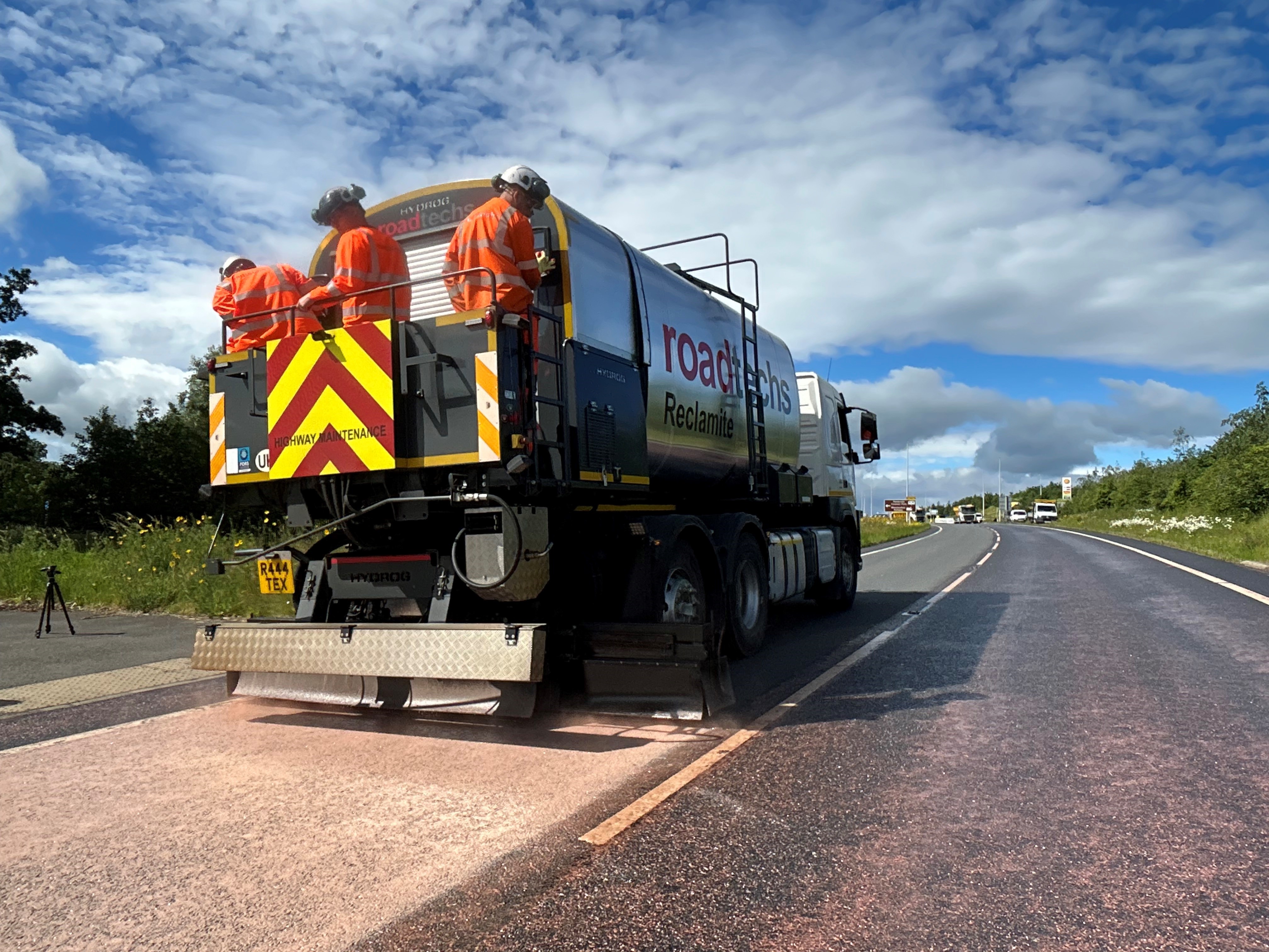 Three adults in hi viz standing on the back of highways vehicle