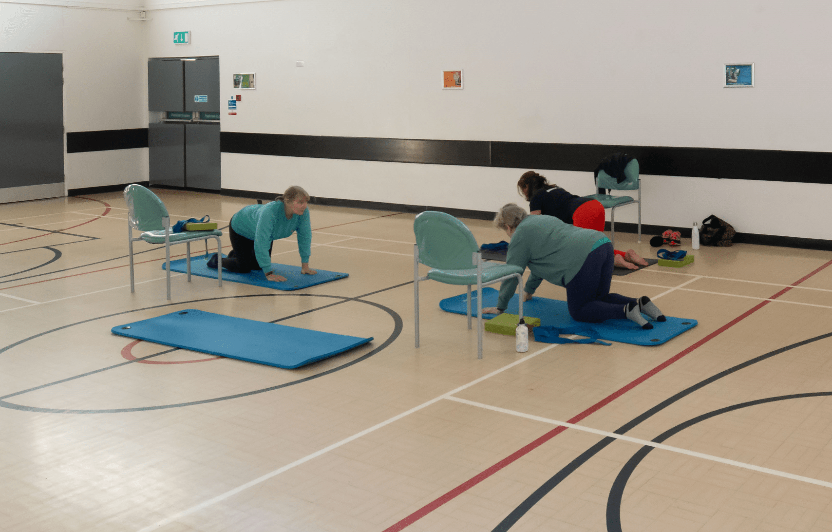 A group of women in yoga poses in the sports hall of the Stockwell Community Wellbeing Hub
