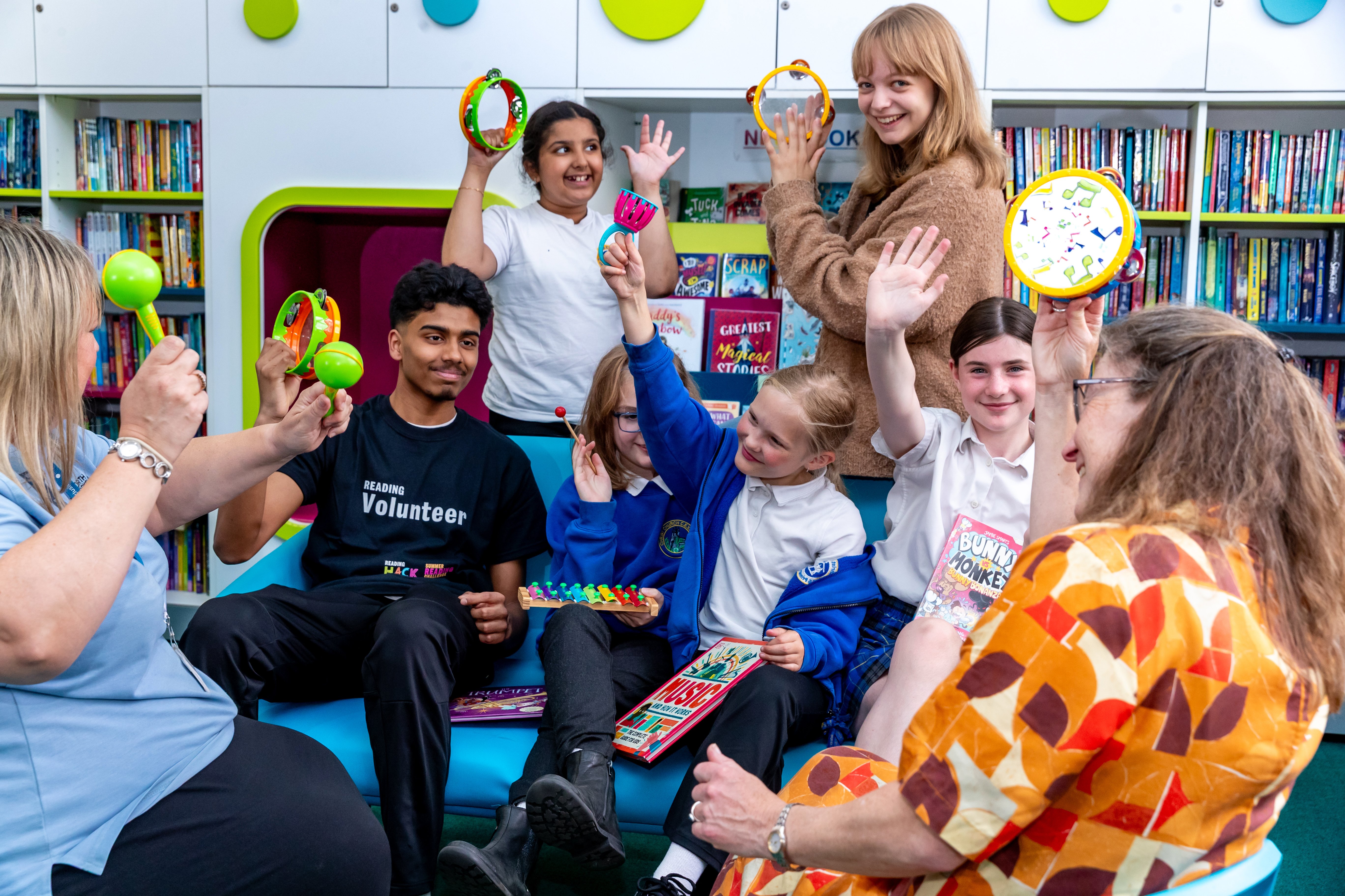 Group of adults and children playing musical instruments surrounded by shelves filled with books