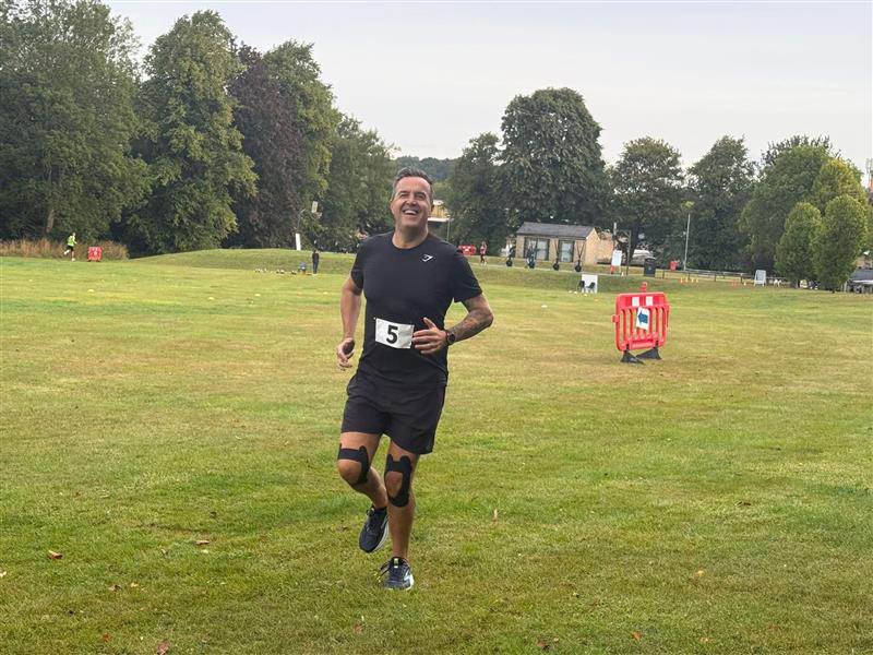 An adult wearing running clothing with the number 5 pinned to their top running across a grass field