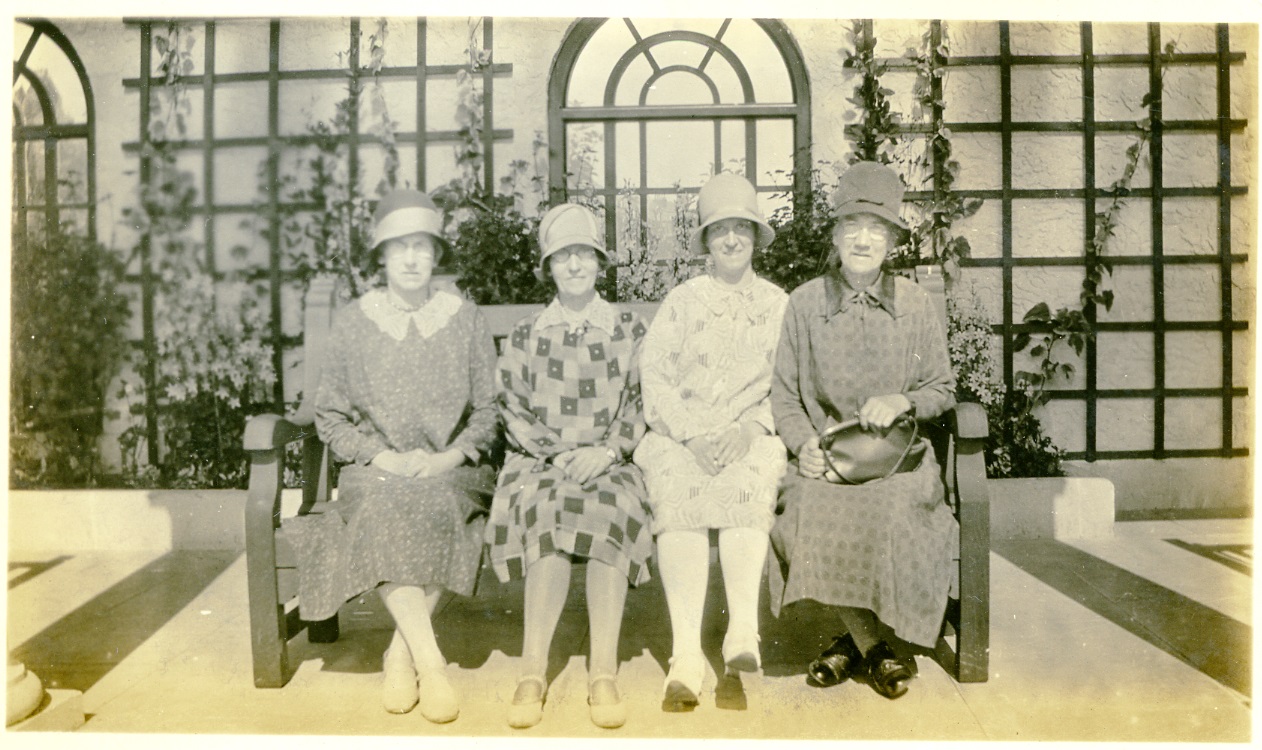 A group of women dressed in bonnets and dresses sit on a bench while enjoying a day out on the coast. From a collection of Scarborough and Whitby photographs dating from 1929.