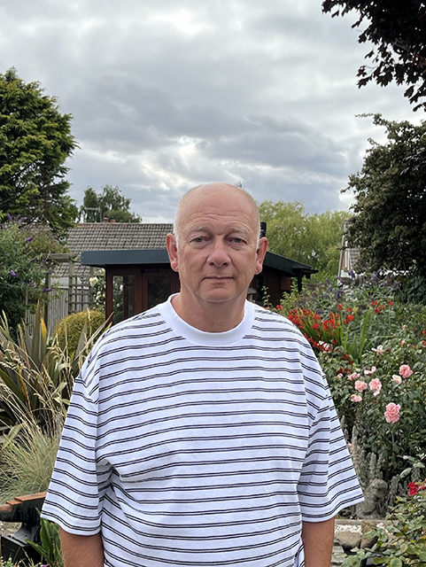 Photo of Mr Goodall standing in his garden with flowers and plants behind him.