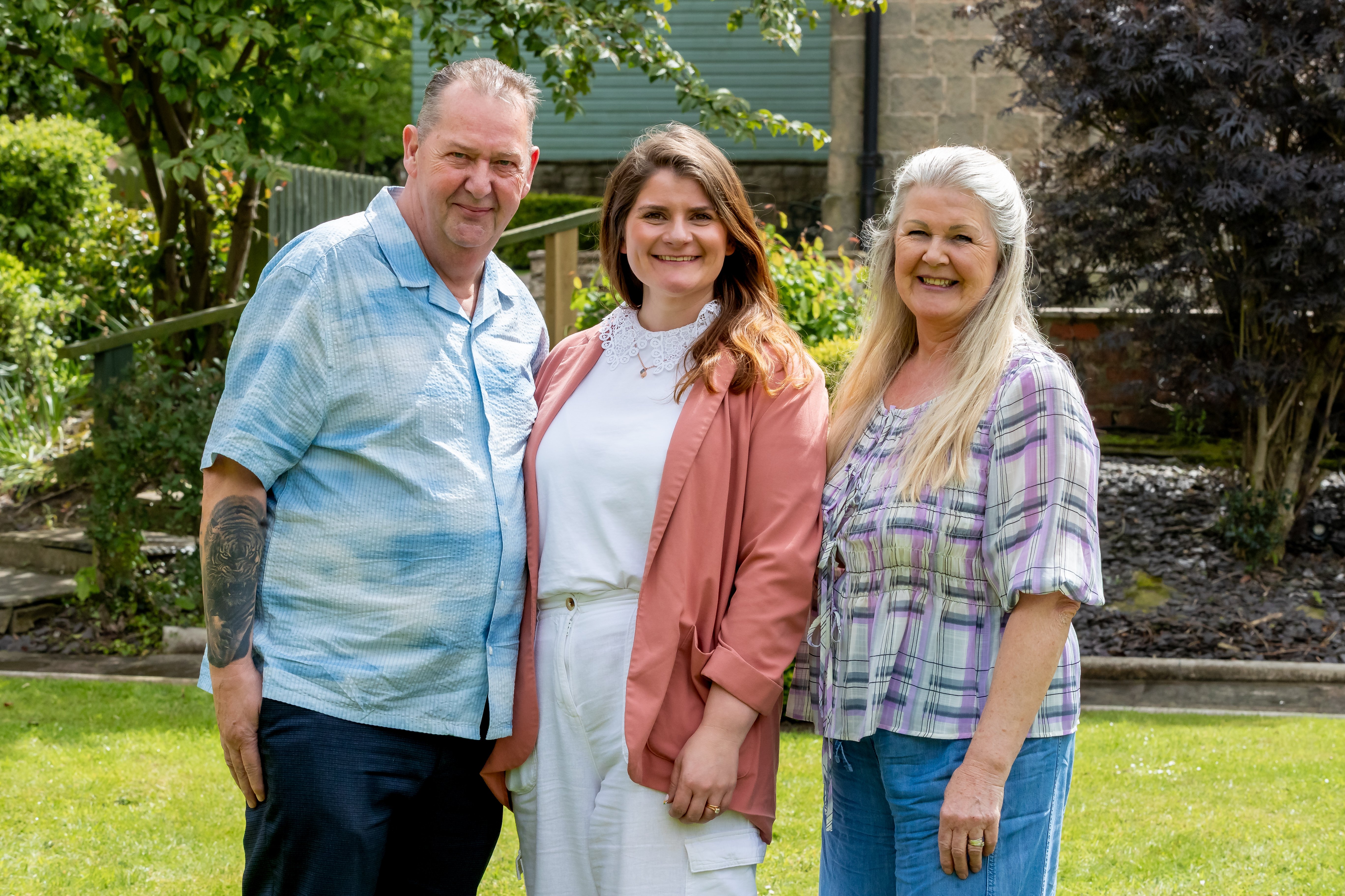 Three adults standing together in a garden