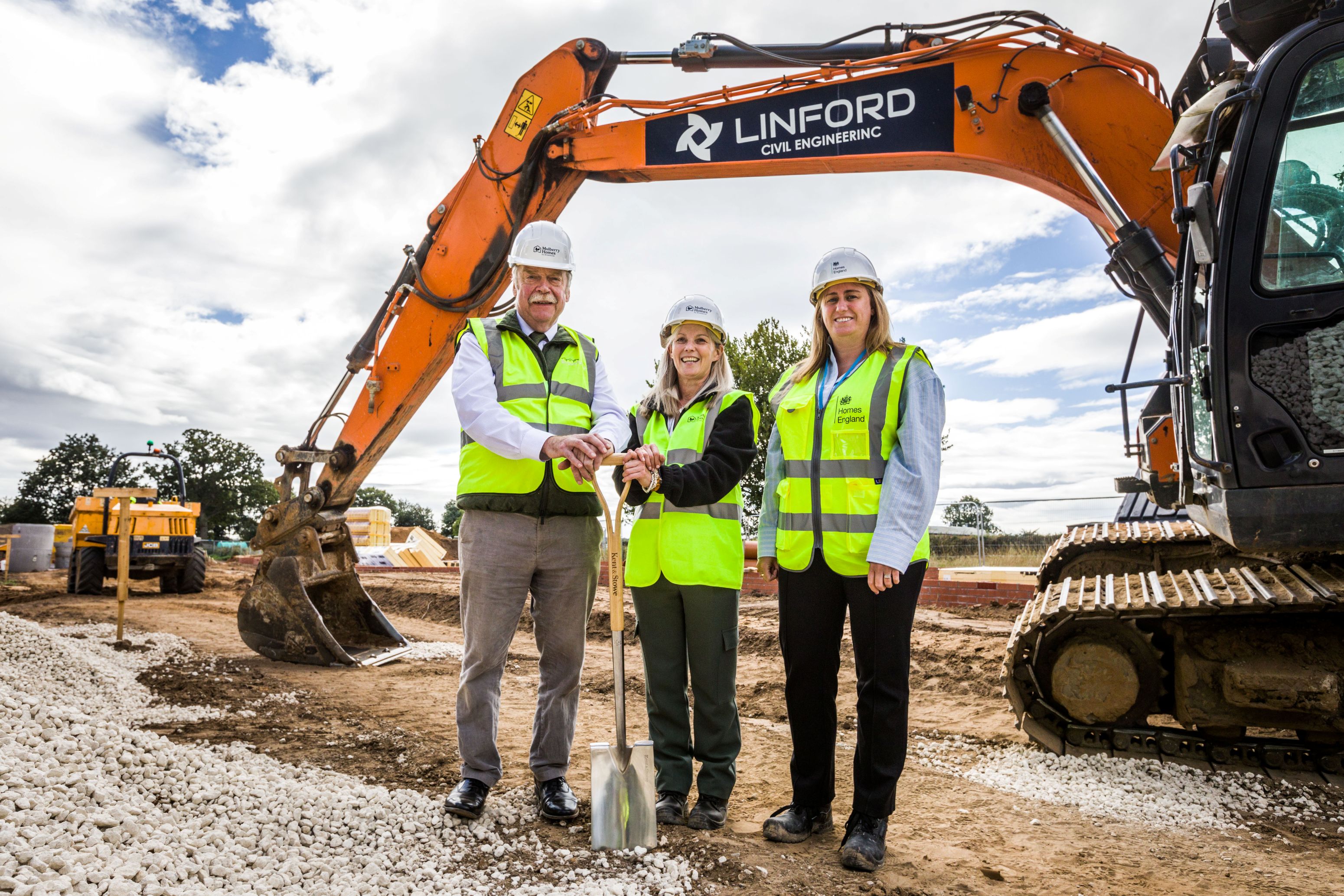 Three people with a spade in front of a digger