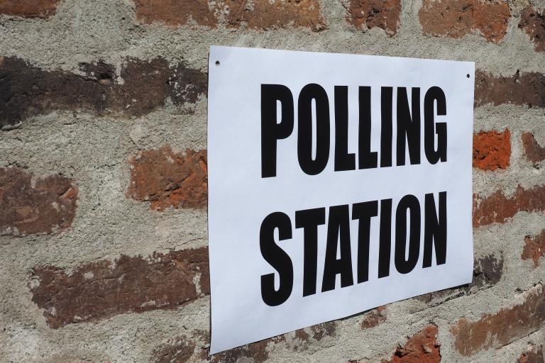 A white sign with the words "Polling station" in black writing on a red brick wall. 