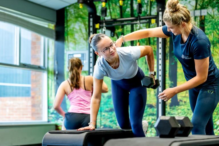 An instructor at a leisure and wellbeing hub helps a woman work out, showing her the correct posture
