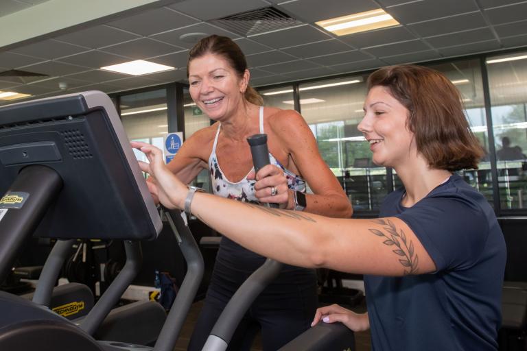 A gym instructor with a lady on a cross trainer