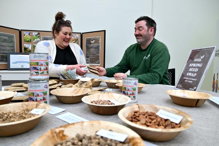 Two people sat behind a table which has bowls of seeds