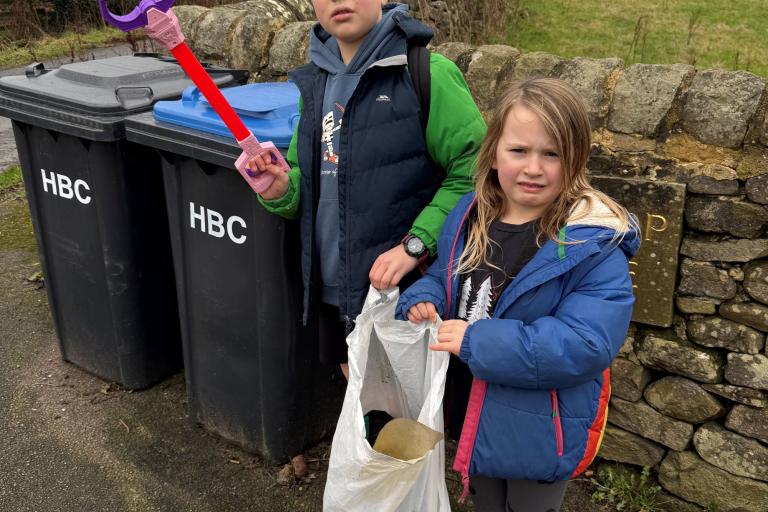 Two children with litter pickers in front of bins