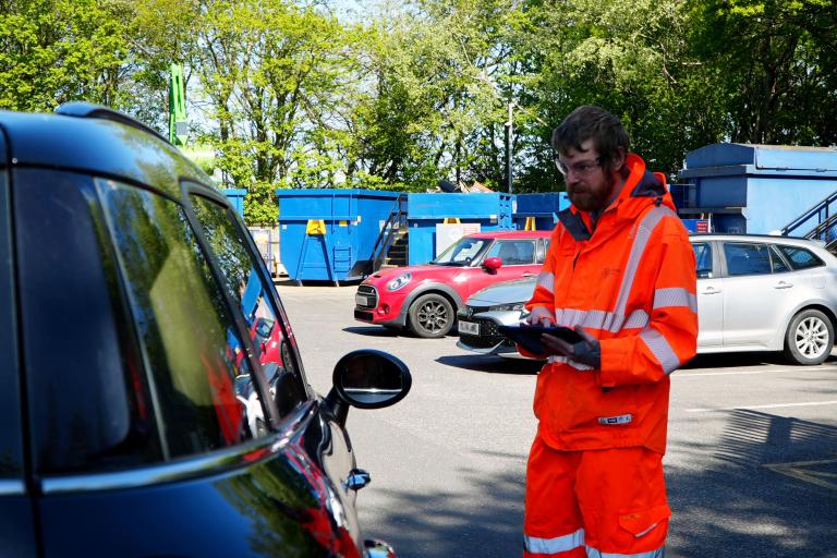 A man in hi viz checking car registration numbers at recycing centres
