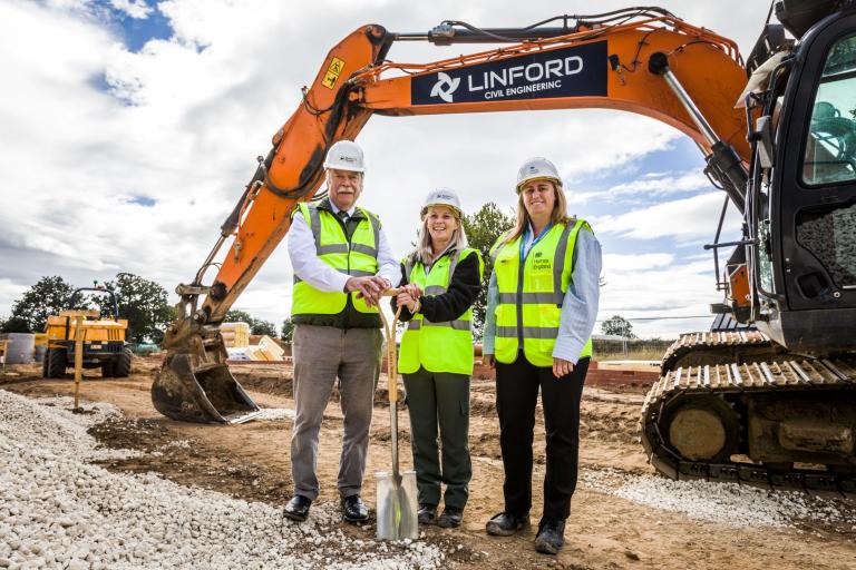 Three people with a spade in front of a digger