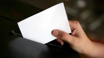 A person putting a ballot paper in a ballot box