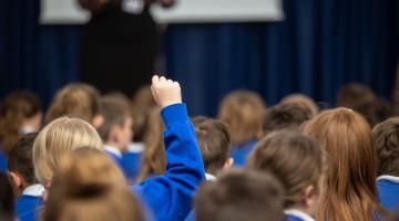 A child with their hand raised in a school assembly 