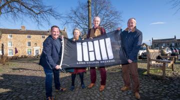 from left to right, Long Course Weekend’s founder and chief executive, Matthew Evans, Flo Grainger, owner of the Old Station Caravan Park, Masham Parish Council vice-chair, Ian Johnson, North Yorkshire Council’s executive member for open to business, Cllr Derek Bastiman pictured with the Long Course Weekend flag in Masham.