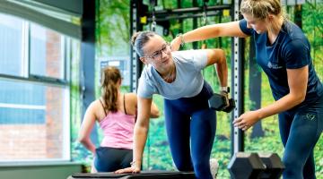 An instructor at a leisure and wellbeing hub helps a woman work out, showing her the correct posture