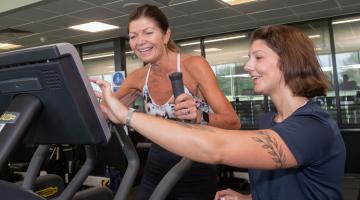 A gym instructor with a lady on a cross trainer