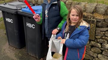 Two children with litter pickers in front of bins