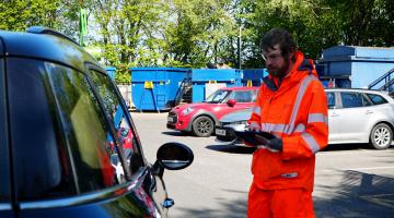 A man in hi viz checking car registration numbers at recycing centres
