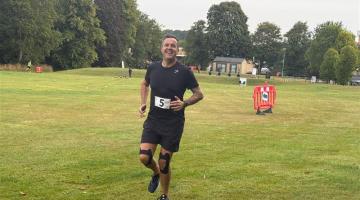 An adult wearing running clothing with the number 5 pinned to their top running across a grass field