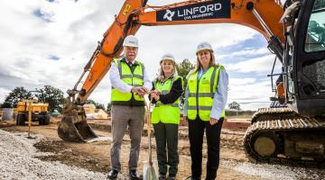 Three people with a spade in front of a digger