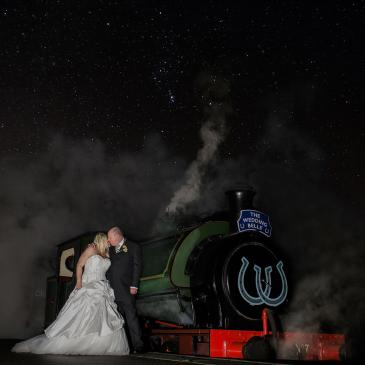 Bride and groom standing on the edge of a train under a starry sky.