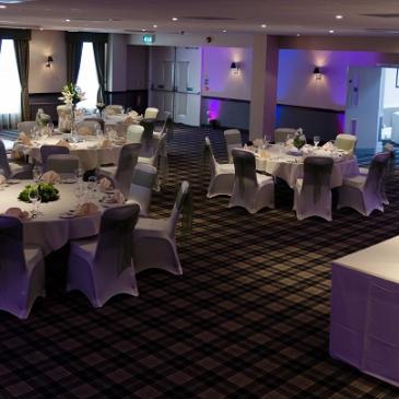 Chairs and tables laid out for a wedding meal under purple lighting.