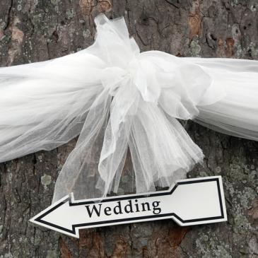 A tree wrapped with ribbon and an arrow pointing towards the wedding venue.