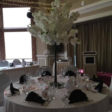 Chairs and table set out for a wedding meal with a floral centre piece.