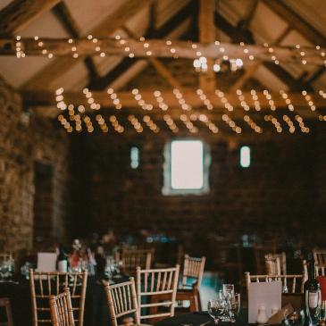 A room decorated with fairy lights and chairs and tables set out for dinner.