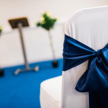 Blue ribbon on the back of a chair with floor decorations out of focus in the background.